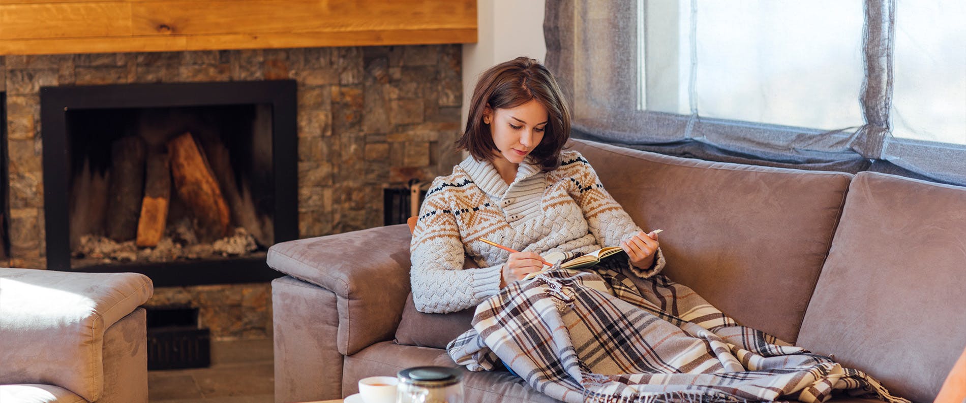Kvinne sitter i en sofa på hytten og leser et magasin