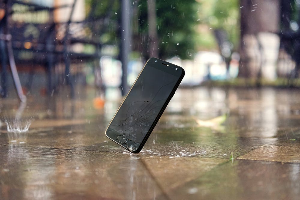 Knust mobil faller i regnet mot steinfliser på bakken