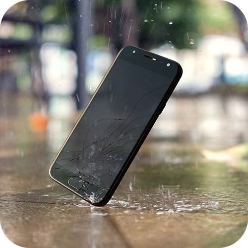 En ødelagt smarttelefon med knust skjerm står oppreist på en våt treoverflate mens regndråper treffer og spretter opp rundt den. Bakgrunnen er uskarp, men man kan skimte trær og en parklignende setting, noe som gir en følelse av at telefonen har blitt mistet utendørs i regnværet.
