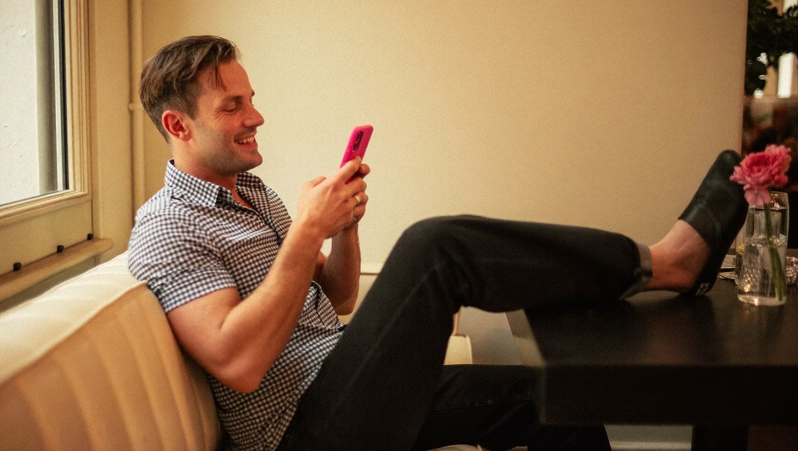 Mann sitter avslappet i en kafésofa med foten oppe og ser på mobilen.